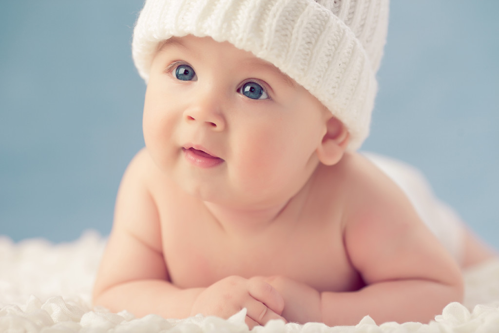 Baby in white winter hat lying on the floor